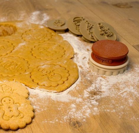 Emporte-pièces personnalisés avec motifs festifs et biscuits réalisés sur plan de travail fariné.