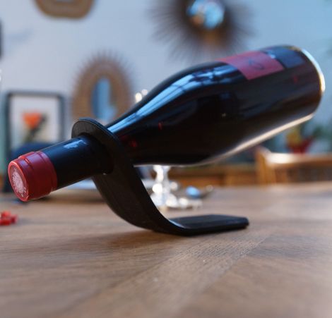 Support à vin noir au design minimaliste maintenant une bouteille de vin rouge en équilibre.