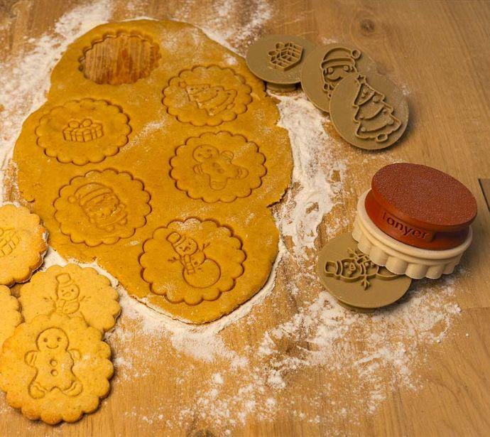Emporte-pièces de Noël avec motifs festifs et biscuits réalisés sur pâte étalée.