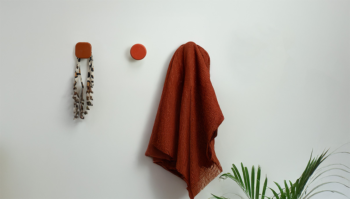 Patères terracotta carrée et ronde sur mur blanc, avec foulard et tissu suspendus.