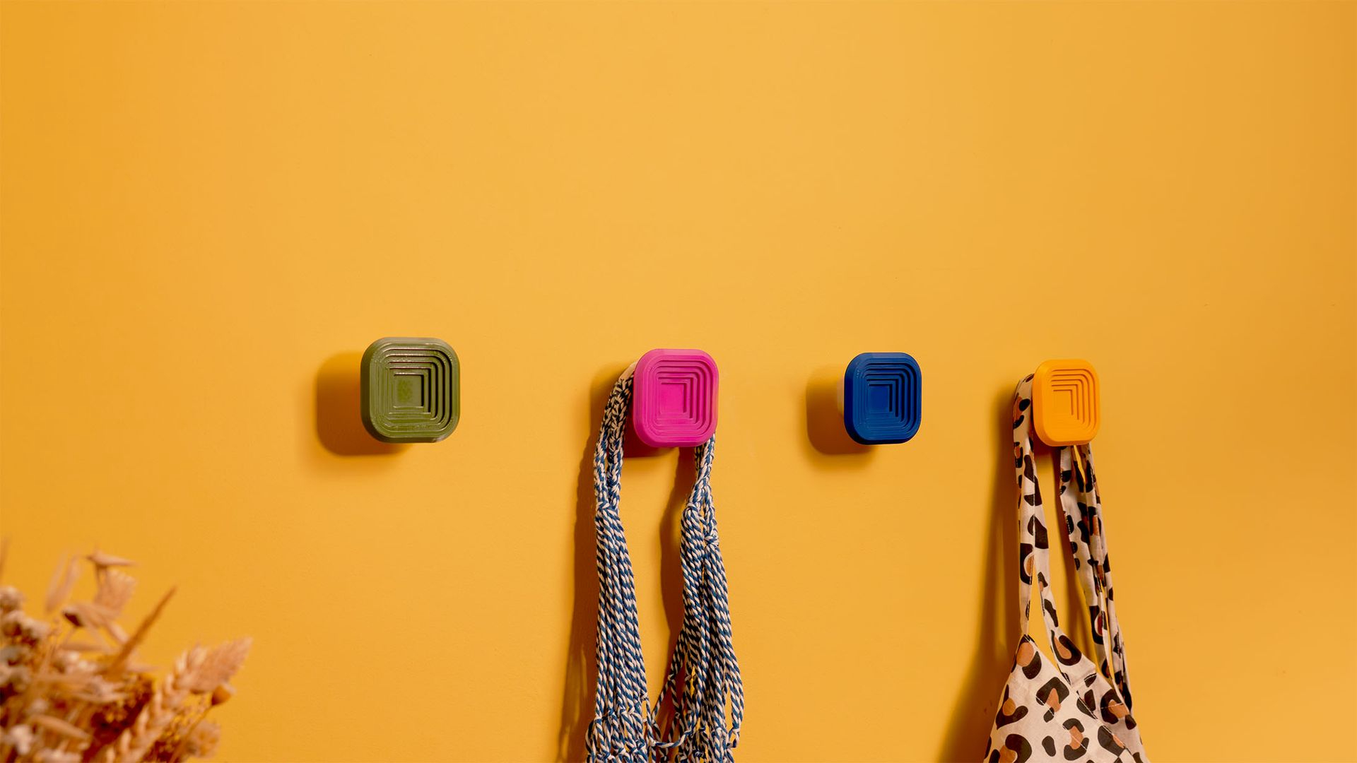 Patères carrées colorées fixées sur mur jaune.