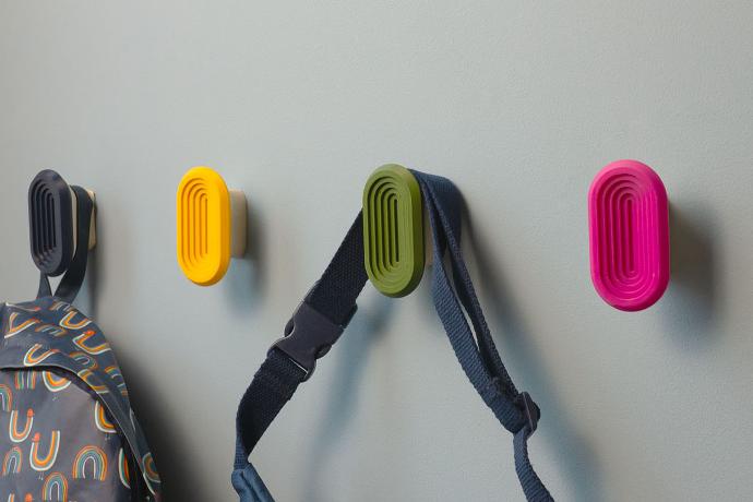 Patères murales colorées fixées sur un mur gris, avec accessoires suspendus.