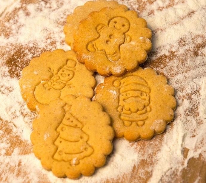Quatre biscuits festifs avec motifs de bonhomme de neige, sapin et père Noël.